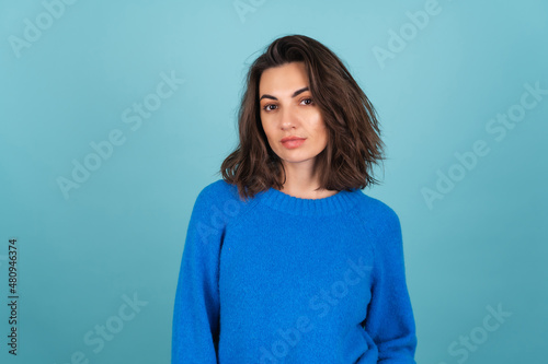 Woman in a blue knitted sweater and natural makeup, curly short hair, look to camera with confident smile