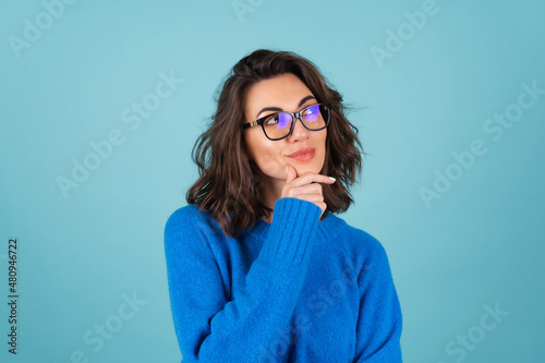 A woman in a blue knitted sweater and natural make-up, curly short hair, glasses on her eyes, looks thoughtfully to the side, meditating