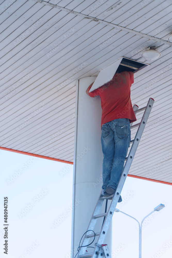 Fototapeta premium A worker on a stepladder checks or repairs something in a hatch on the ceiling