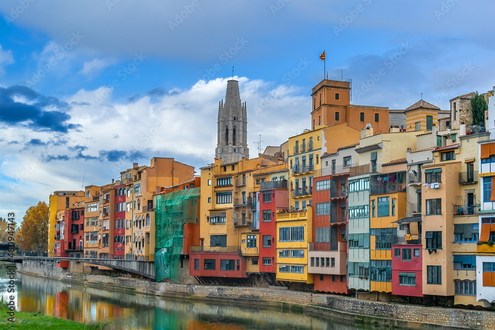 Multicolored colorful buildings of Girona Old Town on the embankment of Onyar river, Spain. Fairy-tale landscape of a Spanish town with the tower of Collegiate Church of St. Felix against the blue sky