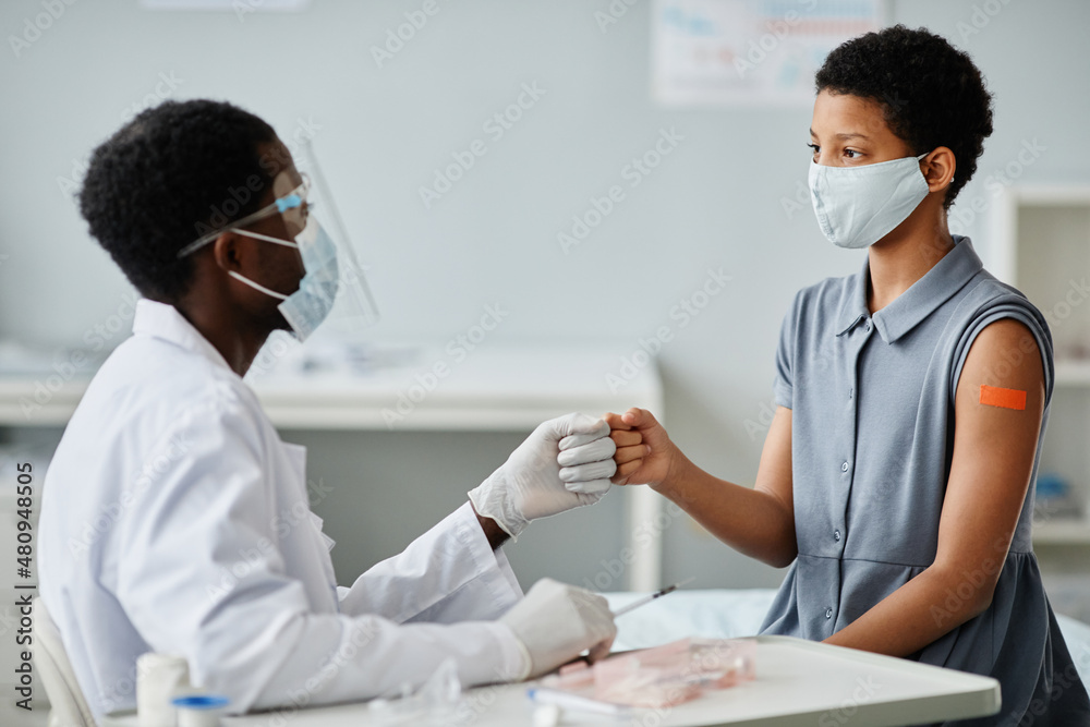 Portrait of teenage African-American girl bumping fists with doctor after getting vaccinated against covid-19 Portrait of teenage African-American girl bumping fists with doctor after getting vaccinated against covid-19