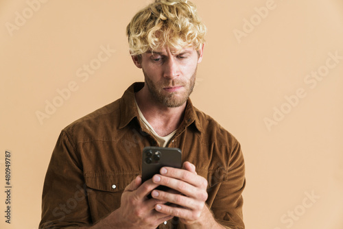 White blonde man wearing shirt frowning and using cellphone © Drobot Dean