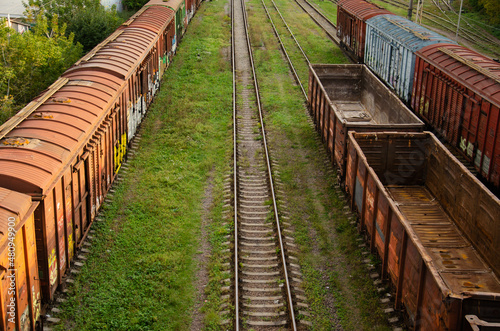 Old freight cars of the train stand on rails. The train stopped at the station in the village. Rusty iron cars and green grass. Railway background with copy space.