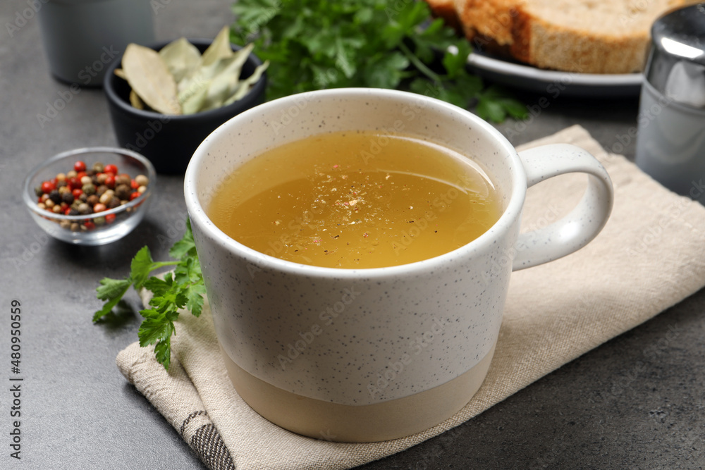Hot delicious bouillon in cup on grey table Hot delicious bouillon in cup on grey table