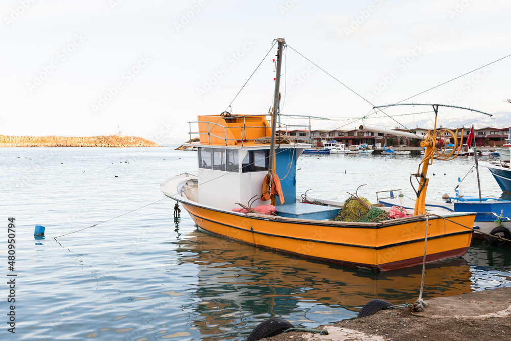 Small yellow fishing boat is moored in fishing harbor