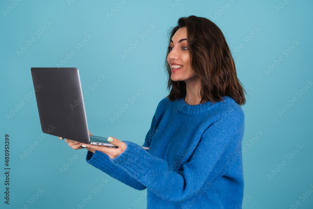Young woman in a knitted sweater isolated holds a laptop, looks at the screen in surprise Young woman in a knitted sweater isolated holds a laptop, looks at the screen in surprise