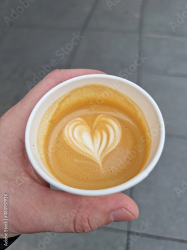 Heart shape on coffee foam. Take away coffee macchiato holds a hand.