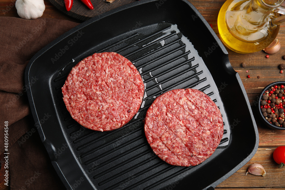 Raw hamburger patties with oil, vegetables and pepper on wooden table, flat lay Raw hamburger patties with oil, vegetables and pepper on wooden table, flat lay