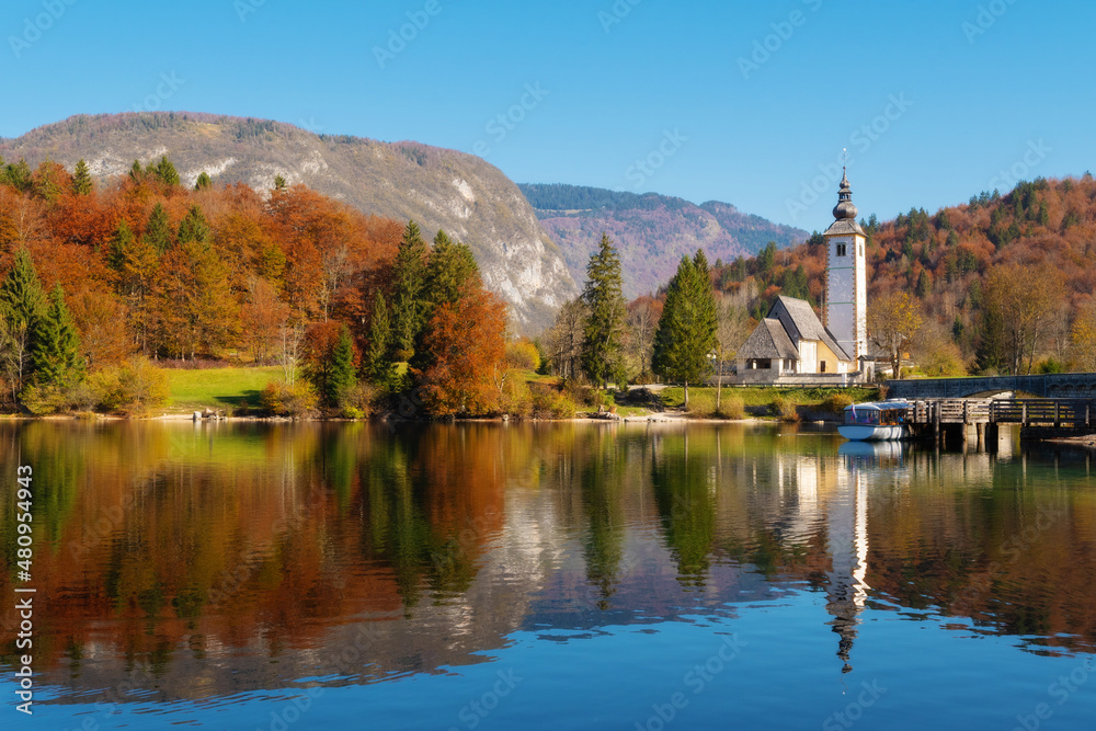 Heartwarming view of lake Bohinj in vibrant autumnal colors and catholic church