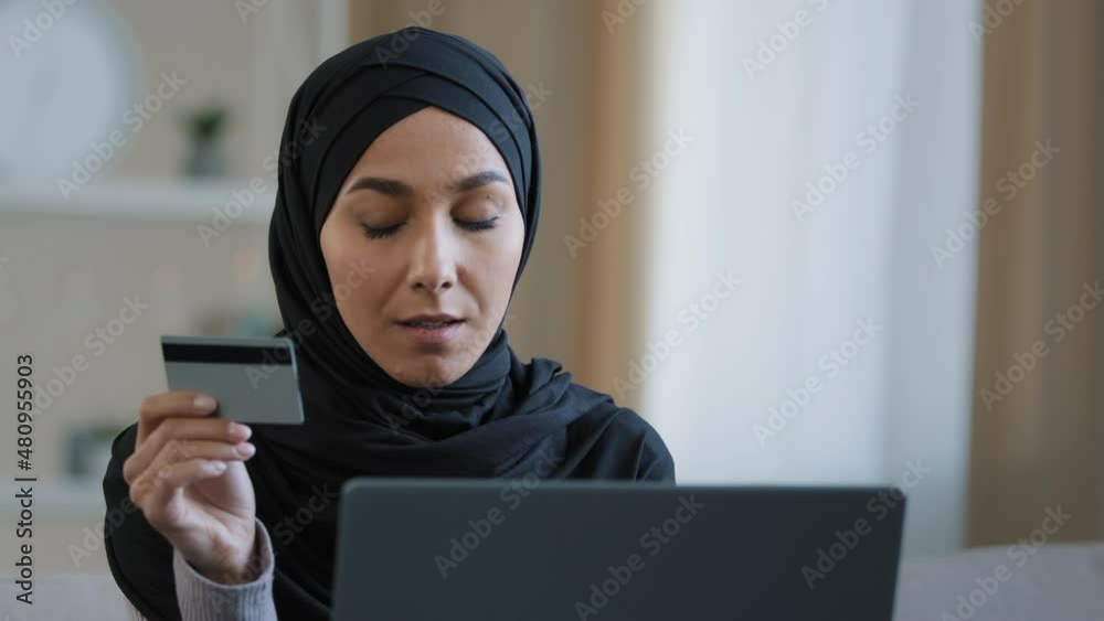 Attractive girl in hijab holding credit card pay online order use banking application on laptop smiling muslim woman shopper rejoices successful purchase make secure money transfer modern tech concept