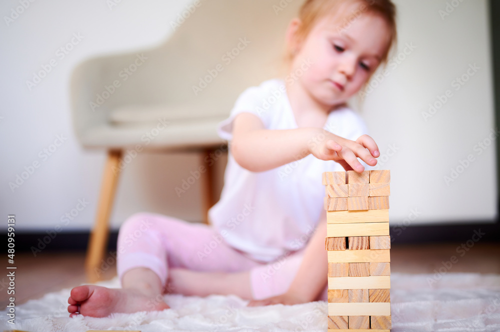 Little cute preschool girl playing jenga on the floor at home and collecting wooden cubes Little cute preschool girl playing jenga on the floor at home and collecting wooden cubes