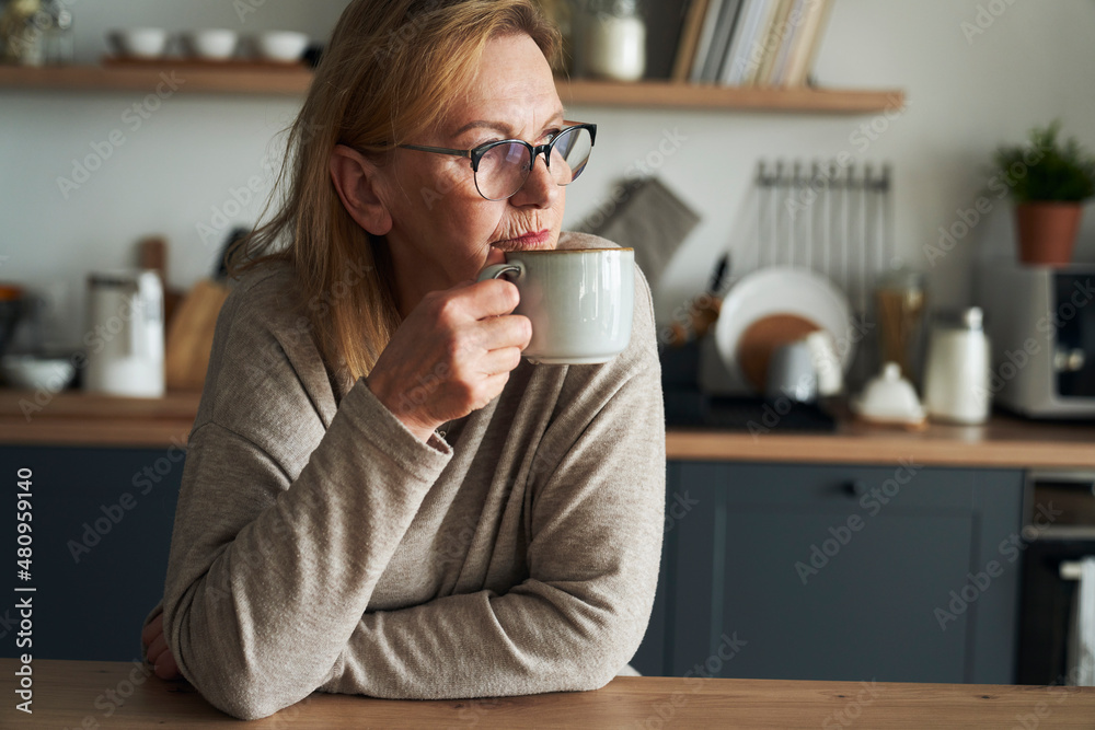 Thoughtful caucasian senior woman sitting in the kitchen, drinking coffee and looking away Thoughtful caucasian senior woman sitting in the kitchen, drinking coffee and looking away