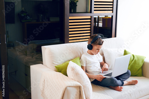 Concentrated schoolboy wearing headphones with laptop play online games at home. Distance learning in quarantine