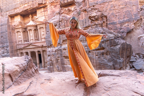 woman dressed in traditional clothes and headscarf staying at the top of rock on the background is Petra palace Jordan