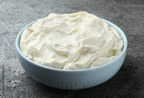 Bowl of tasty cream cheese on grey table