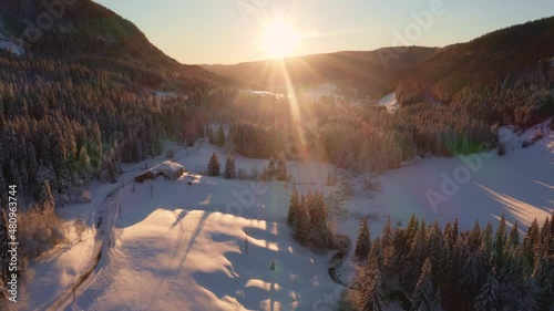 Survol image aérienne face au soleil couchant d’une vallée de montagne recouverte de neige. Lumière chaude rasante sur la foret de sapins du Jura (Valserine, Mijoux) photo