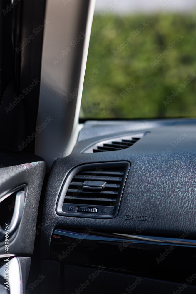 Close up of plastic car air ventilation grills from air condition system in a compact Japanese car. Selective focus points. Seeing a front glass windshield showing a park in the morning. Close up of plastic car air ventilation grills from air condition system in a compact Japanese car. Selective focus points. Seeing a front glass windshield showing a park in the morning.
