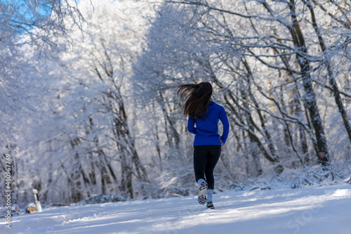 Sportswoman running in nature at snowy winter day. Winter fitness concept.