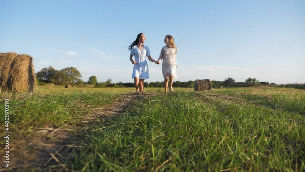 Friendly family. Mother and daughter holding hands at sunset running in the meadow. Happy mom and daughter walk holding hands towards the sunset in summer. Freedom happiness concept. Friendly family. Mother and daughter holding hands at sunset running in the meadow. Happy mom and daughter walk holding hands towards the sunset in summer. Freedom happiness concept.