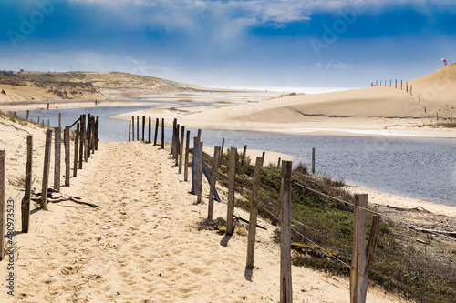 Accès à une plage par un sentier sableux bordé de piquets le long d'une rivière côtière. Réserve naturelle du Courant d'Huchet, Landes, France