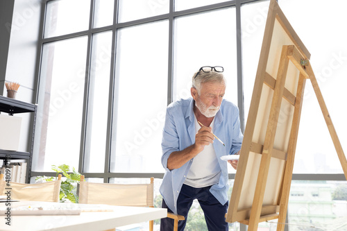senior man painting a picture from paintbrush in free time © offsuperphoto