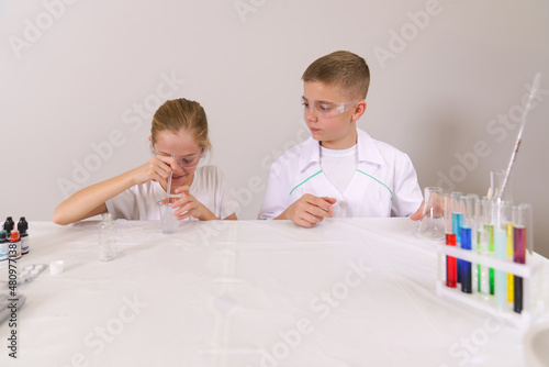 a white boy and a white girl do a chemical experiment on a white table