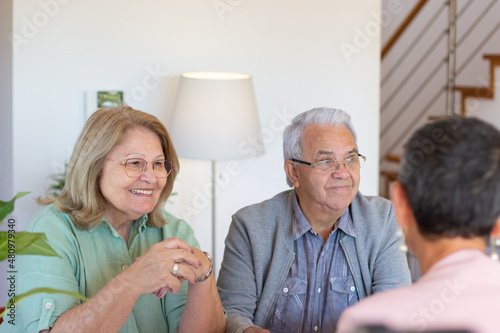 Content elderly couple signing documents. Smiling family looking at woman with short hair in pink suit sitting at table. Real estate, business, work concept