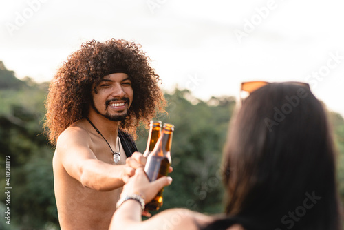 Leinwand Poster un hombre latino sonriente de cabello rizado brindando con cerveza con una mujer