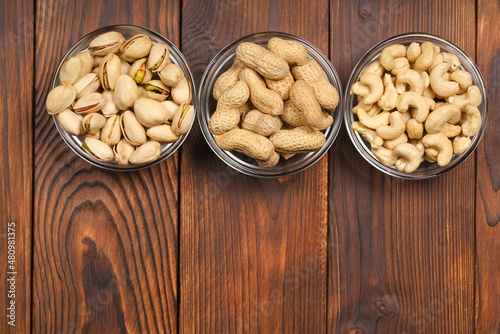 pistachio nuts, peanuts and cashews in glass cups on a wooden table. Space for text.