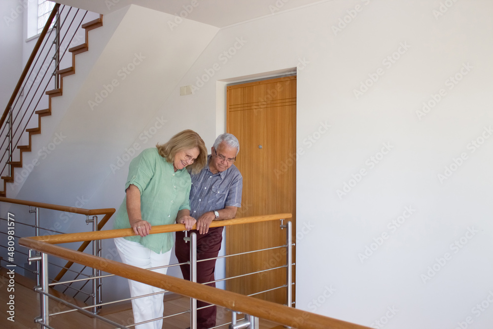 Happy retired family at moving day. Elderly man and woman standing at second floor, looking at their new home. Real estate, purchase, family concept