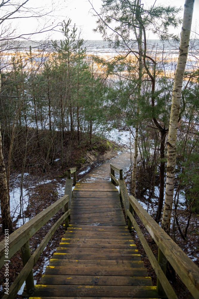 Obraz premium Wooden stairs on the footpath by the sea with yellow warning signs in winter.