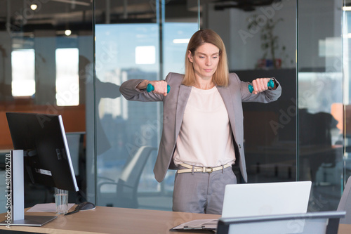 Fototapeta Naklejka Na Ścianę i Meble -  Beautiful and happy woman doing sports exercises in the office at work, during a break, business woman monitors health engaged in fitness