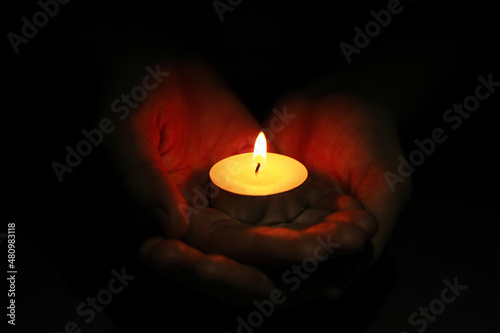 Woman holding burning candle in darkness, closeup