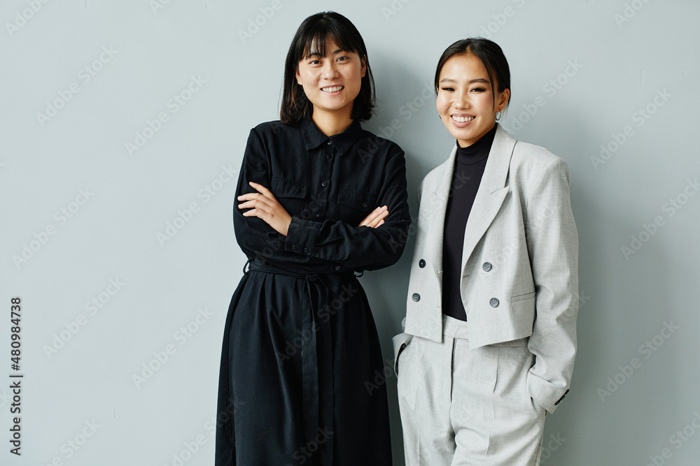 Minimal waist up portrait of two young Asian businesswomen smiling at camera, copy space