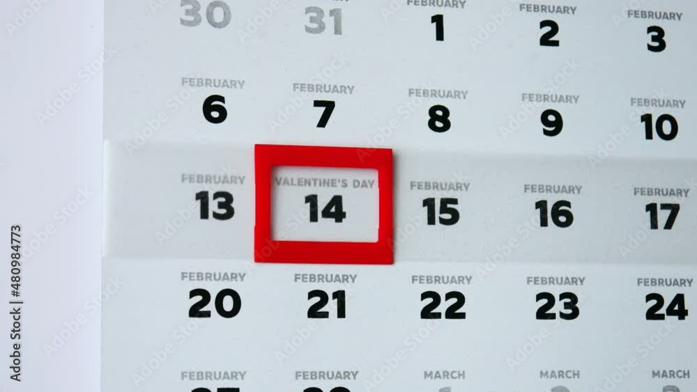 Close-up of a February page of the wall calendar and a mans finger moves a red cursor to Valentine's Day date Close-up of a February page of the wall calendar and a mans finger moves a red cursor to Valentine's Day date