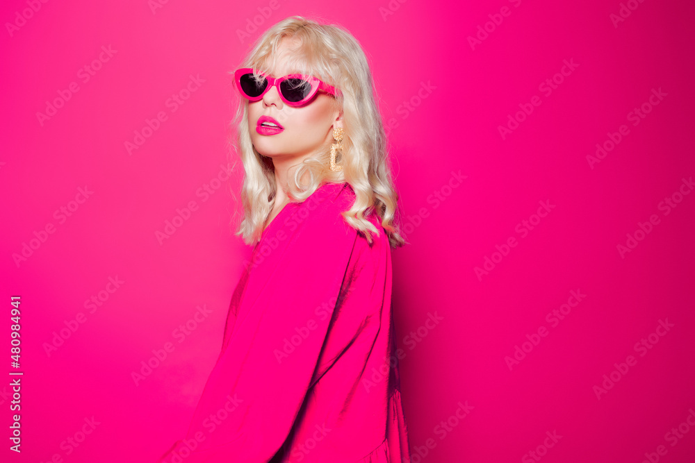 The blonde poses on a pink background in stylish pink glasses and a dress. Girl model posing, bright photo fashion and style, gold jewelry 80s and 90s The blonde poses on a pink background in stylish pink glasses and a dress. Girl model posing, bright photo fashion and style, gold jewelry 80s and 90s
