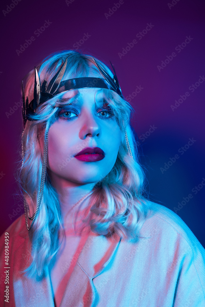 Queen in a silver crown, trendy stylish neon photo. The woman is all in jewelry and bijouterie. Red blue light. Evening make-up, red lips and shadows in sparkles