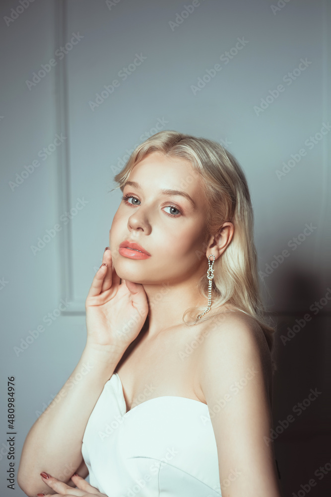 Naklejka premium Portrait of a bride, a woman in a white dress with a beautiful pink make-up. Long earrings as a decoration for a wedding, jewelry for the bride