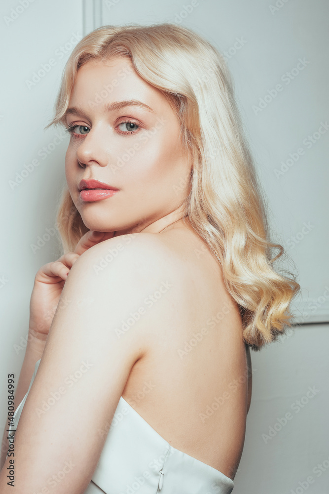 Gorgeous portrait of a blonde woman in a wedding dress. A girl with soft pink makeup looks at the camera. Bride before the wedding