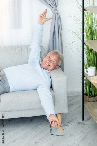 Happy senior man. Couch relaxing. Vacation holiday. People leisure. Joyful mature male employee having work break resting on sofa at home living room.