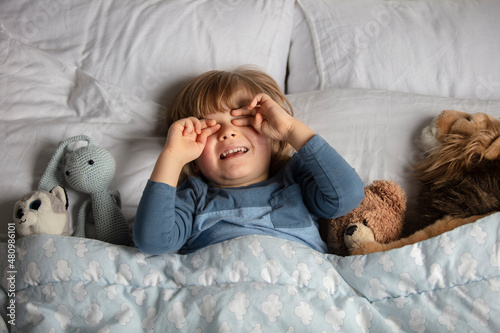 The child was scared before going to bed. Night terrors in a child. The kid covers his face with his hands in a fear. Children's experiences. Boy in the bed. View from above. Sad psychological state.
