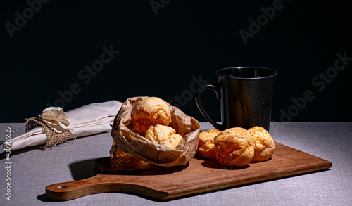 lanche delicioso com pão de queijo sobre uma tábua, caneca preta de louça e guardanapo photo