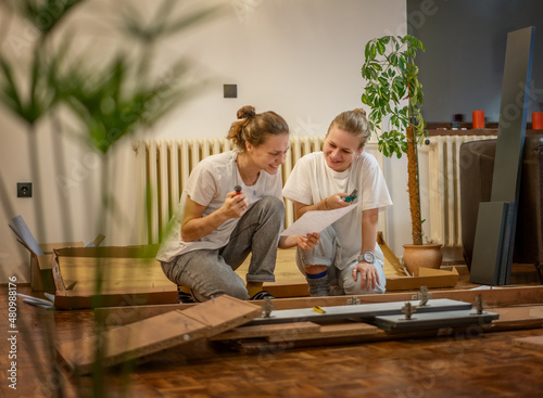 Obraz na plátne Two young women girlfriends or lesbian couple assembling furniture in their new home