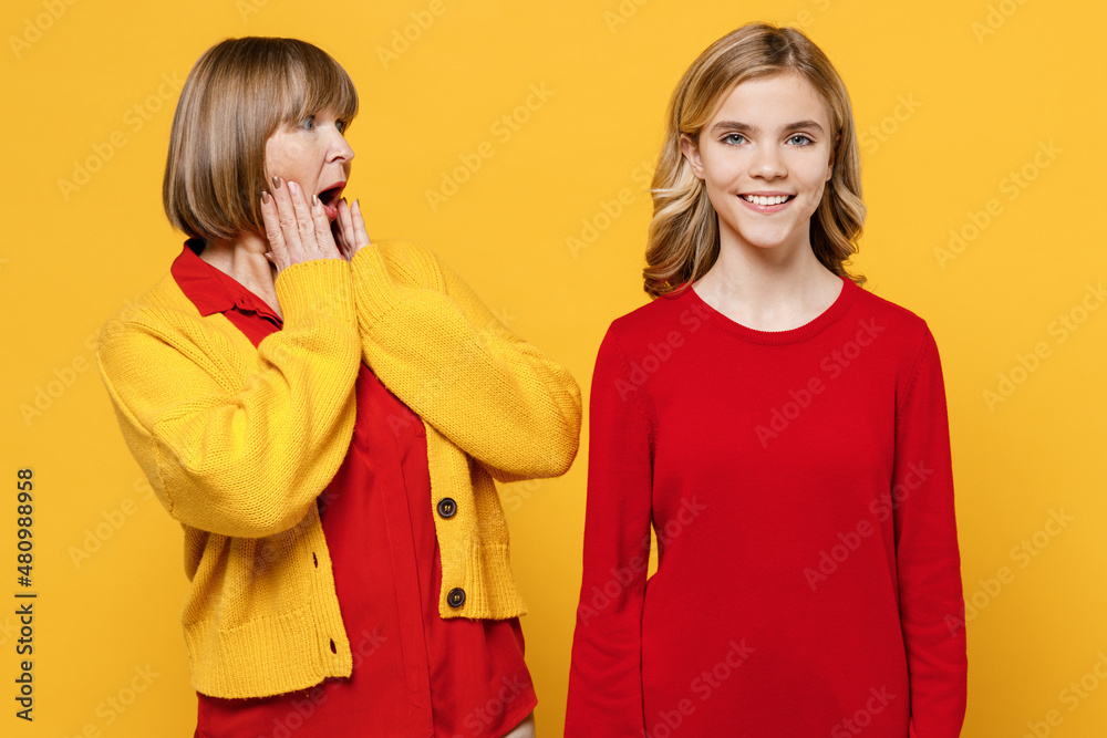 Happy shocked surprised woman 50s in red shirt have fun with teenager girl 12-13 years old. Grandmother look at granddaughter hold face isolated on plain yellow background. Family lifestyle concept. Happy shocked surprised woman 50s in red shirt have fun with teenager girl 12-13 years old. Grandmother look at granddaughter hold face isolated on plain yellow background. Family lifestyle concept.