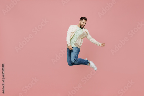 Full body young expressive singer happy caucasian man 20s in trendy jacket shirt jump high play guitar gesture isolated on plain pastel light pink background studio portrait. People lifestyle concept. © ViDi Studio