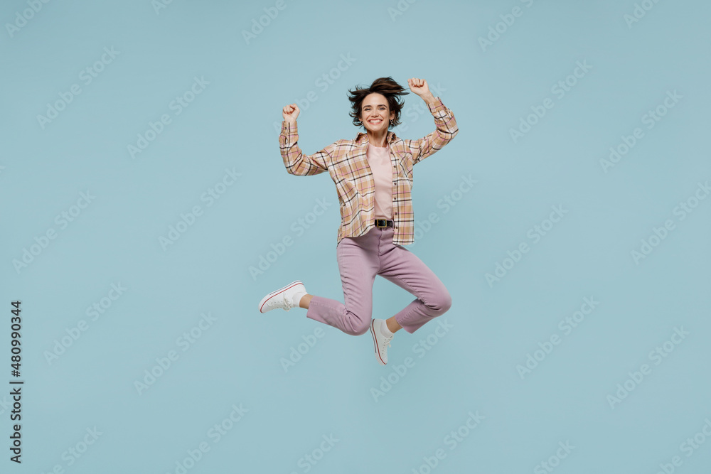 Full body young excited happy woman 20s wear casual brown shirt jump high do winner gesture clench fist isolated on pastel plain light blue color background studio portrait People lifestyle concept