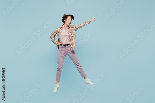 Full body young excited amazed woman 20s wearing casual brown shirt jump high point index finger aside on workspace area mock up isolated on pastel plain light blue color background studio portrait