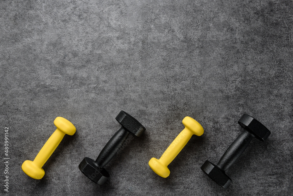 Black and yellow dumbbells on a dark textural background with copy space. Flat lay composition with dumbbells. Black and yellow dumbbells on a dark textural background with copy space. Flat lay composition with dumbbells.