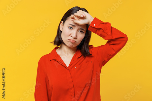 Sick ill young woman of Asian ethnicity 20s wears orange shirt put hands on head rub temples having headache suffering from migraine feel bad seedy isolated on plain yellow background studio portrait.