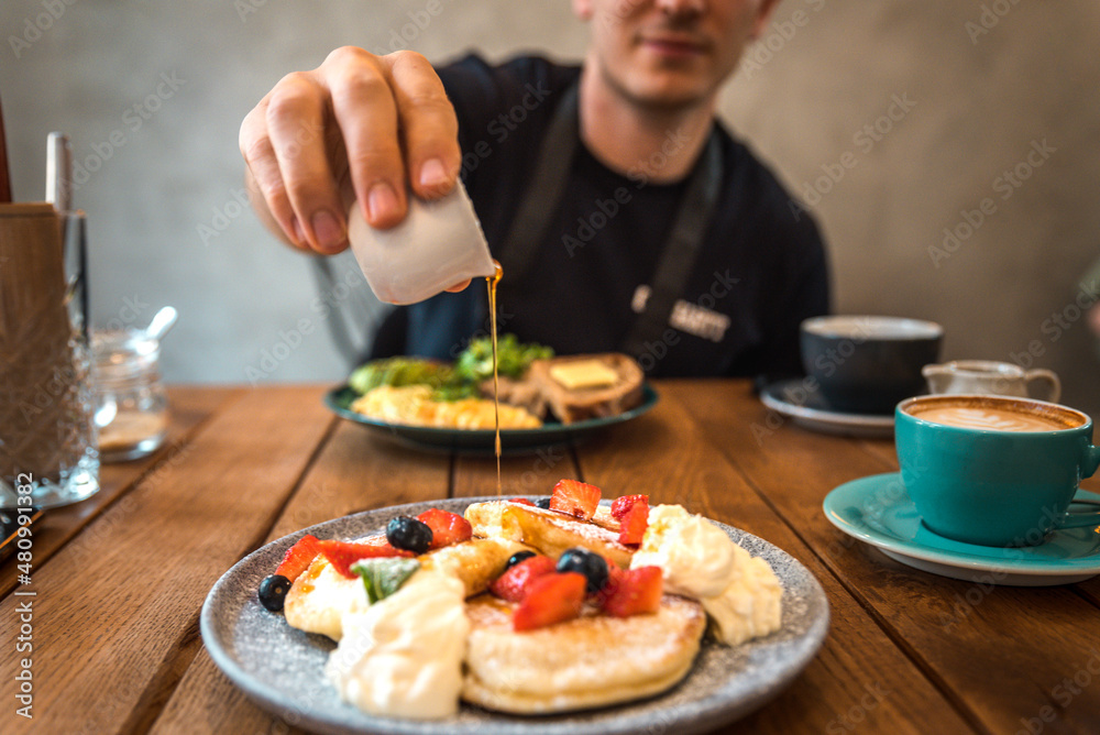 Maple syrup on pancakes with strawberries, blueberries and whipped cream. Brunch in a café. Maple syrup on pancakes with strawberries, blueberries and whipped cream. Brunch in a café.